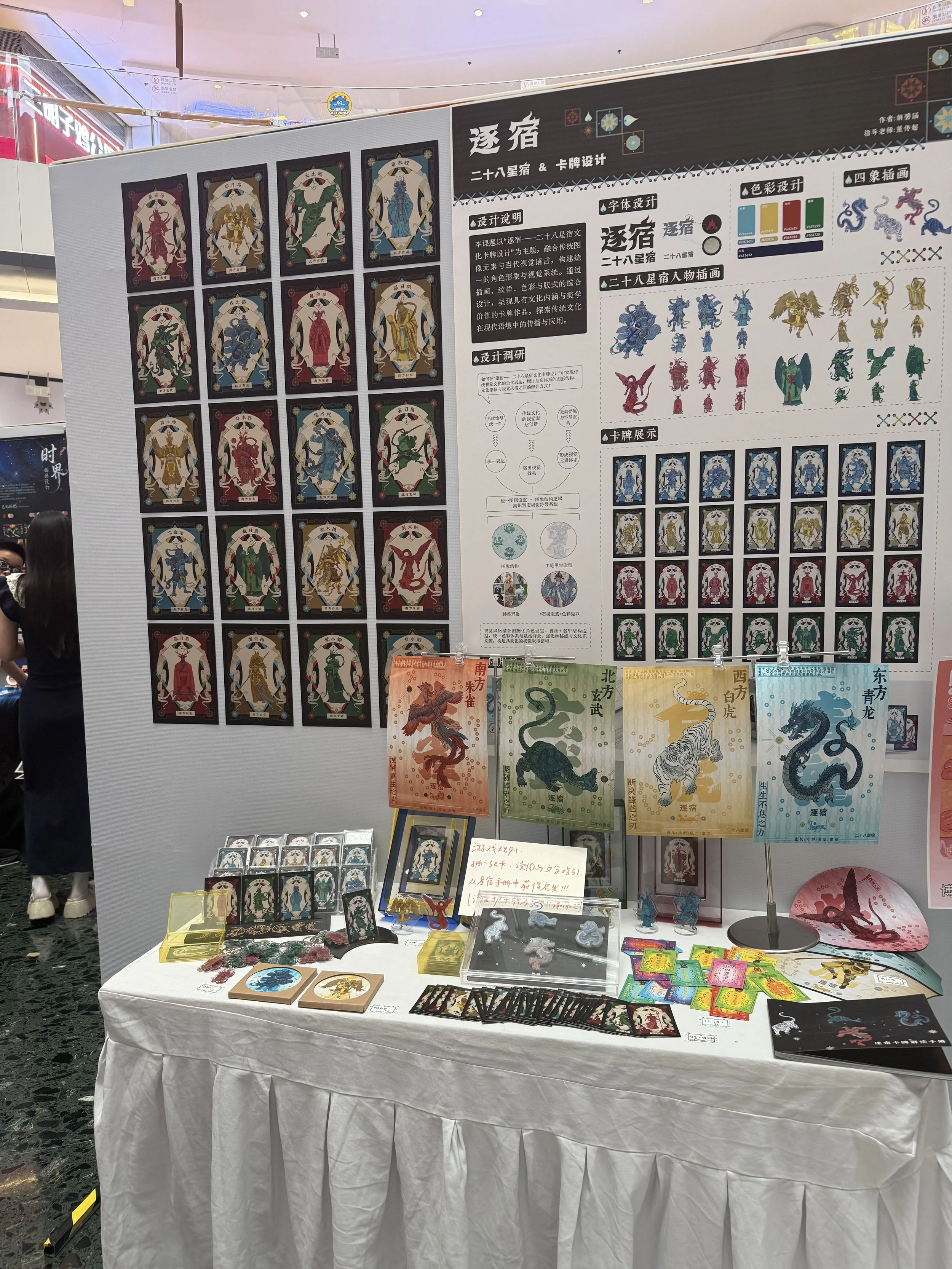 Display booth with various cards, flags, and artwork of Chinese zodiac signs, featuring dragons and other mythical creatures. The backdrop includes detailed Chinese text and illustrations of zodiac animals.