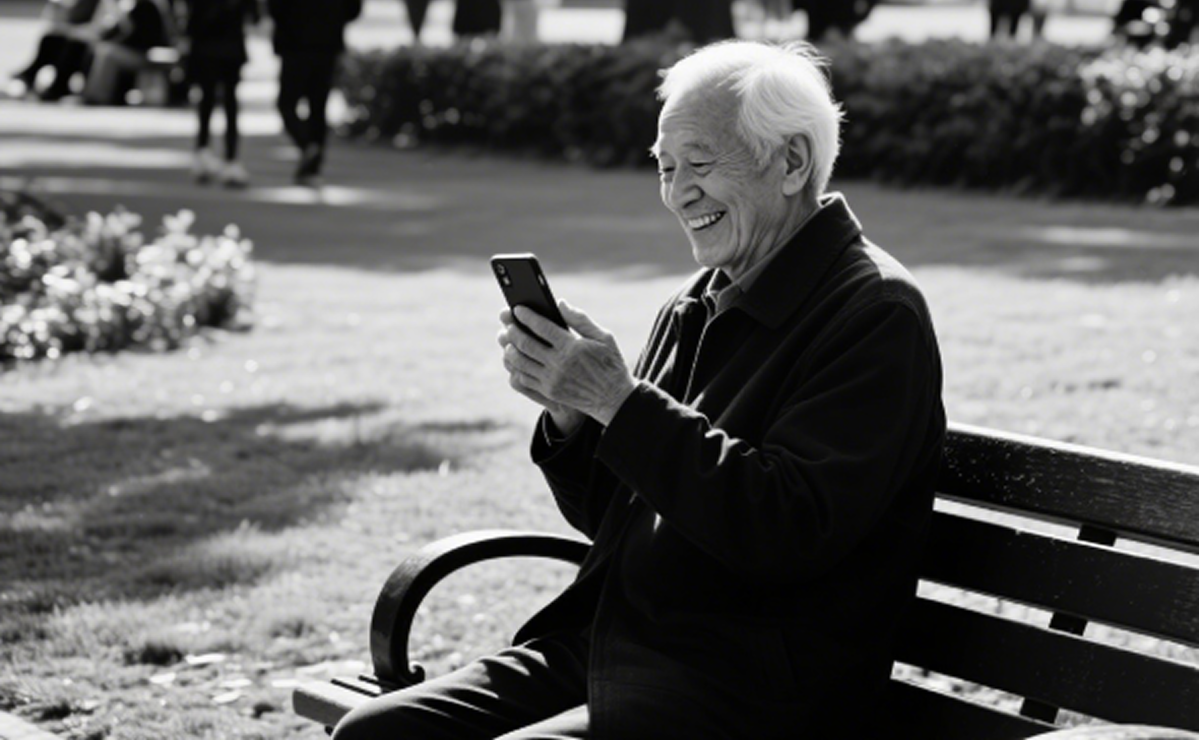 An elderly man with white hair sitting on a park bench, smiling while looking at his smartphone. In the background, there are people walking and some bushes.